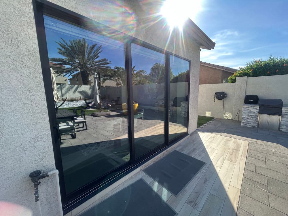 Modern patio with large glass sliding doors, sunlight reflecting, and outdoor furniture in view.