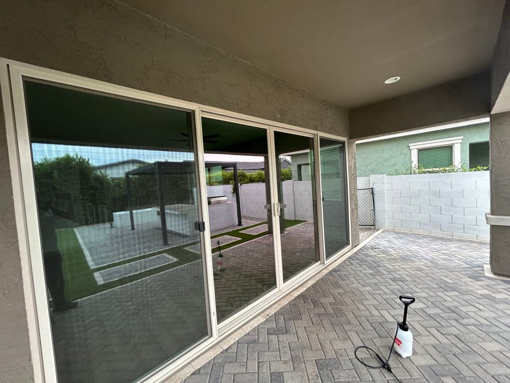 Modern patio area with sliding glass doors, paver flooring, and green landscaping.